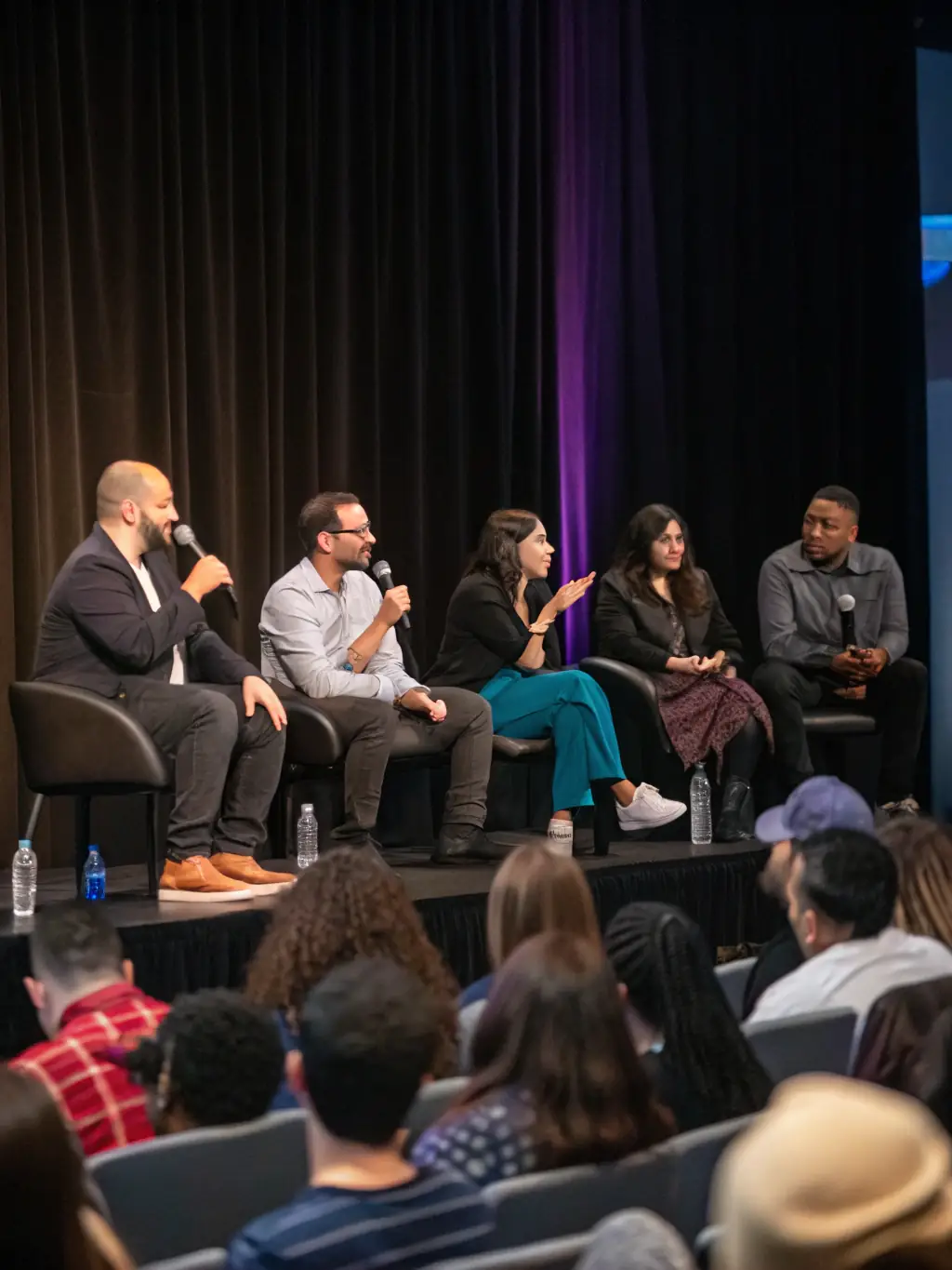 A photograph of a panel discussion at a conference, with several speakers seated at a table, answering questions from the moderator and audience.